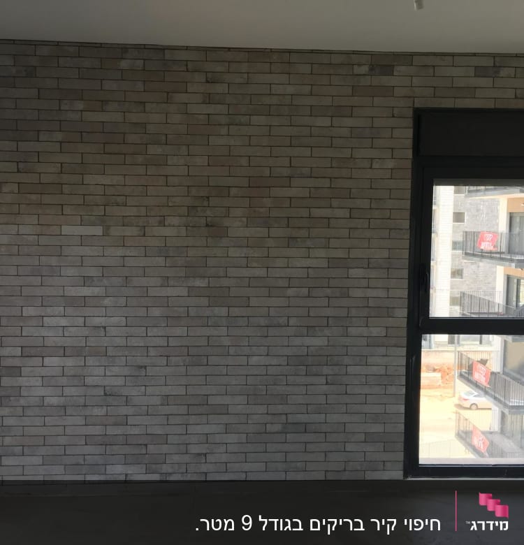 קיר לבנים אפור וחלון גדול בחדר ריק